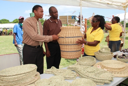 (L-R) Junior Minister of Trade and Industry on Nevis Hon. Dwight Cozier, standing beneath a handmade wooden underwater themed wind chime takes a close look at a hand woven basket with Permanent Secretary in the Ministry of Trade Mr. Dwight Morton and General Manager of the Nevis Craft House Ms. Doretta Daniel. They are standing next to a variety of straw items on display