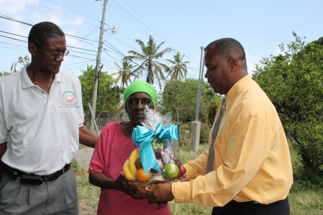 Director of the Department of Agriculture Keithley Amory (right) and Permanent Secretary in the Ministry of Agriculture on Nevis Eric Evelyn present a fruit basket to retired Agriculture Worker Claudina Claxton of Brown Hill on May 21, 2014, in appreciation of her contribution to the development of agriculture on Nevis as part of Agriculture Awareness Month