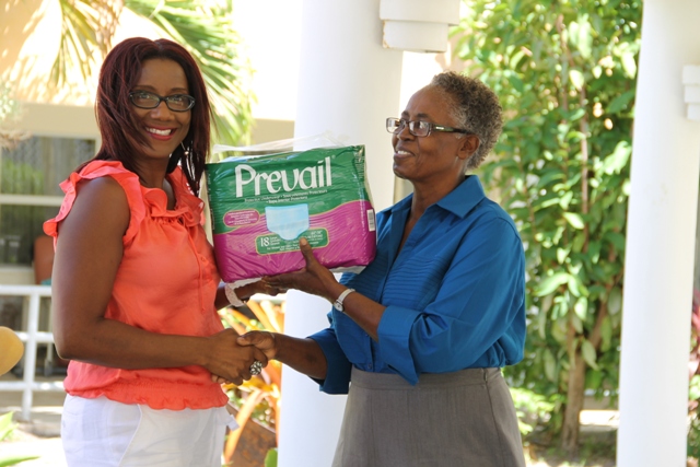 Vice President of the Nevis Association of South Florida, Avonelle Hanley officially handing over a donation of adult protective underwear to the Supervisor of the Flamboyant Nursing Home, Ena Sutton at the Flamboyant Nursing Home on May 19, 2014